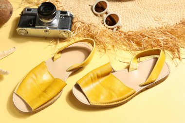 Güneş gözlüklü sandaletler, kamera ve sarı arka planda hasır şapka.