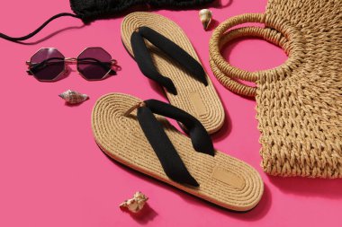 Pembe arka planda mayo, güneş gözlüğü ve çantalı terlikler.