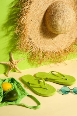 Çantalı terlikler, güneş gözlüğü ve yeşil duvarın yanında hasır şapka.