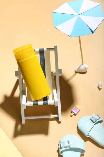 Creative composition with miniature deckchair, umbrella and sunscreen on color background