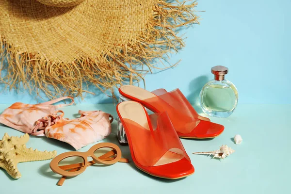 Pair of high heeled sandals with sunglasses, swimsuit and wicker hat on blue background