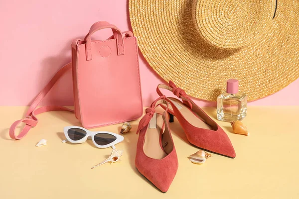 Pair of high heeled sandals with sunglasses, bag and wicker hat near pink wall
