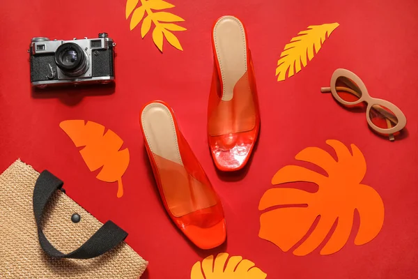 Pair of high heeled sandals with sunglasses, camera and wicker bag on red background