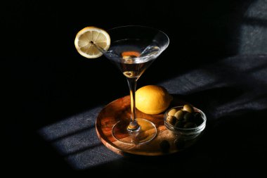 Bir bardak lezzetli martini, koyu arkaplanda limon ve yeşil zeytin.