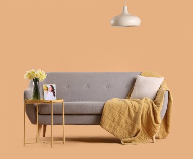 Konforlu gri kanepe ve bej arka planda narsis çiçekleri olan kahve masası.