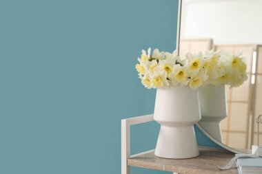Vazoda narsis çiçekleri ve mavi duvarın yanında ayna olan raf ünitesi.