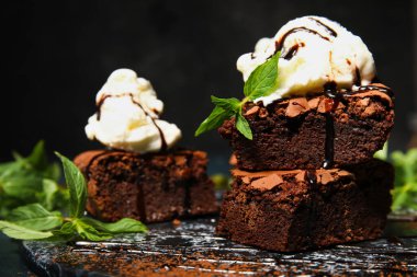 Lezzetli çikolatalı brownie ve koyu arkaplanda dondurma parçaları olan bir pano.