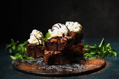 Lezzetli çikolatalı brownie ve koyu arkaplanda dondurma parçaları olan bir pano.