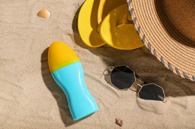 Güneş kremi şişesi ve kumdaki plaj aksesuarlarıyla yaratıcı kompozisyon.