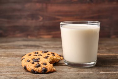 Bir bardak süt ve arkaplanda çikolata parçacıkları olan ısırılmış kurabiye.