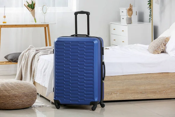 薄暗い部屋のベッドの近くの青いスーツケース — ストック写真