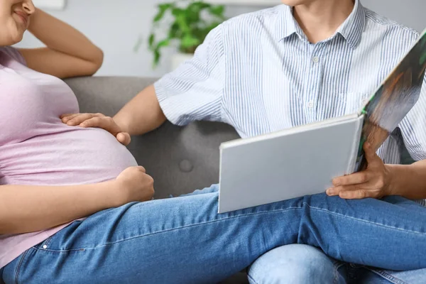 若いです妊娠中のカップル読書本にソファに家 クローズアップ — ストック写真