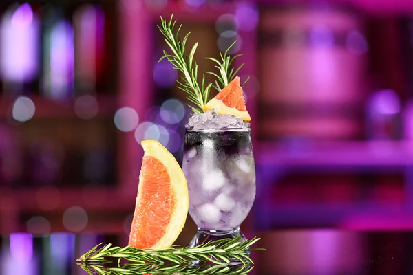 stock image Glass of purple gin and tonic with grapefruit and rosemary on table in bar against blurred background