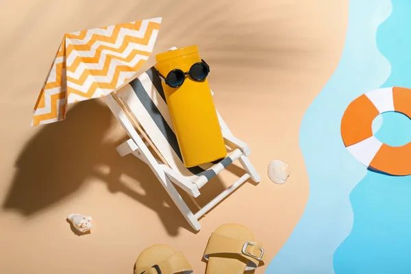 Creative composition with miniature deckchair, umbrella and sunscreen on beach near water
