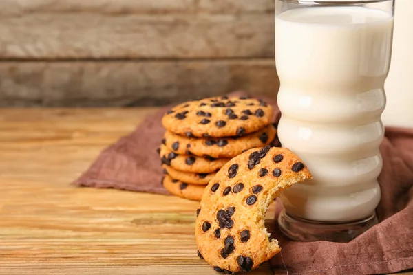 Bitten cookie with chocolate chips and glass of milk on wooden background