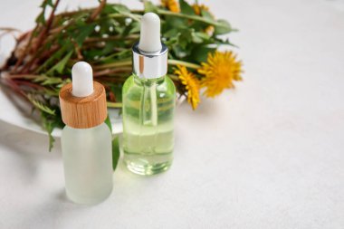 Kozmetik yağlı şişeler ve beyaz arka planda karahindiba çiçekleri.