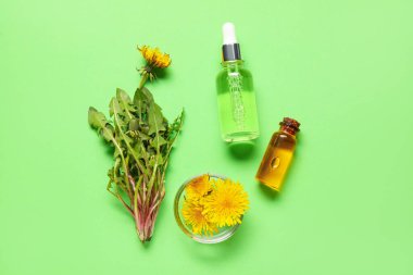 Kozmetik yağlı şişeler ve yeşil arka planda bir kase karahindiba çiçeği.