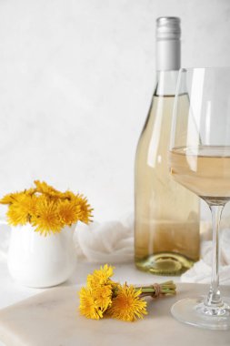 Beyaz masada bir şişe ve bir bardak karahindiba şarabı.