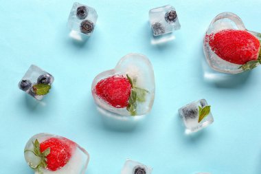 Taze çilek ve yaban mersini. Mavi arka planda buzda dondurulmuş.