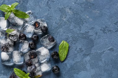 Mavi zemin üzerinde buz küpleriyle dondurulmuş taze yabanmersini.