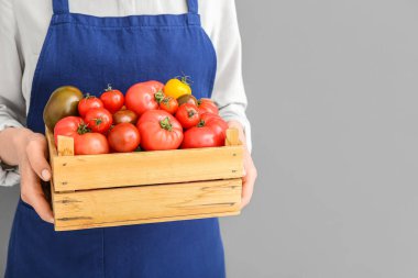 Gri arka planda farklı taze domatesli ahşap kutu tutan kadın, yakın plan.