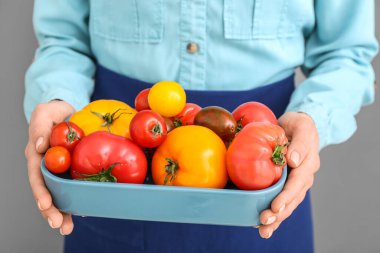 Gri arka planda farklı taze domatesleri olan bir kadın, yakın plan.