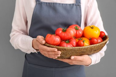 Gri arka planda farklı taze domatesleri olan hasır kaseli kadın, yakın plan.