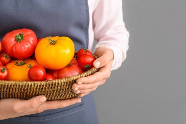 Gri arka planda farklı taze domatesleri olan hasır kaseli kadın, yakın plan.