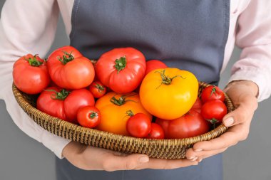 Gri arka planda farklı taze domatesleri olan hasır kaseli kadın, yakın plan.