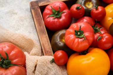 Gri arka planda farklı taze domatesler olan ahşap kutu, yakın plan.