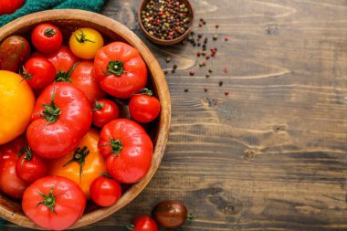 Ahşap arka planda farklı taze domateslerle dolu bir kase.