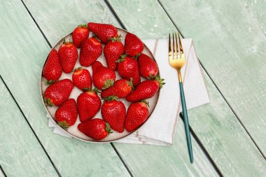 Yeşil ahşap arka planda taze çilekli tabak.