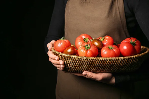 stock image Woman holding wicker bowl with different fresh tomatoes on black background, closeup