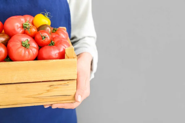 Kobieta Trzymająca Drewniane Pudełko Różnymi Świeżymi Pomidorami Szarym Tle Zbliżenie — Zdjęcie stockowe