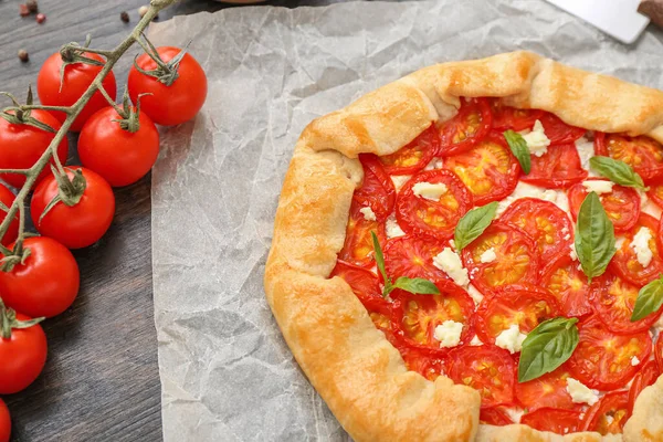 stock image Baking paper with tasty tomato galette and basil on wooden background