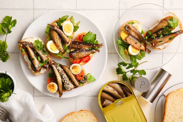 stock image Plates of tasty sandwiches with canned smoked sprats on white tile background