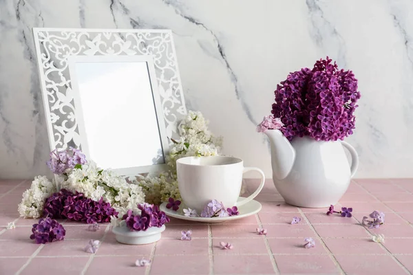 Cup of tea with lilac flowers and frame on pink tile near grunge white wall