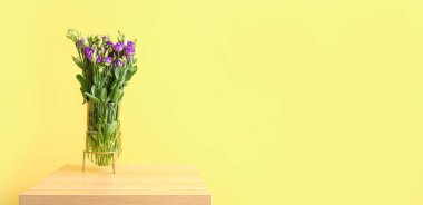 Sarı duvarın yanındaki masada güzel Eustoma çiçekleri olan vazo. Tasarım için pankart