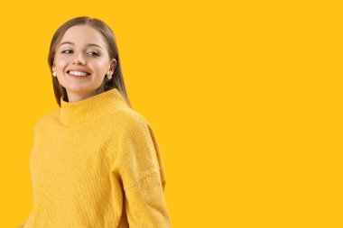 Fashionable young woman in knitted sweater on yellow background