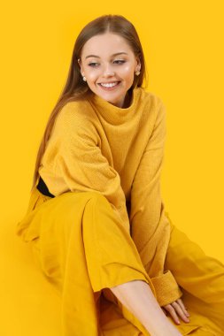 Fashionable young woman in knitted sweater and skirt on yellow background