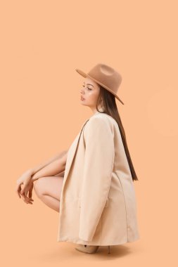 Fashionable young woman in stylish clothes and hat on beige background