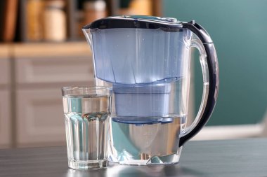 Modern filtre sürahi ve bir bardak su mutfaktaki siyah masada.