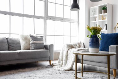 Büyük pencerenin yanında rahat kanepeleri ve kahve masası olan parlak bir oturma odası.