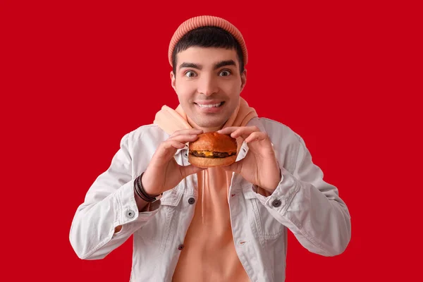 Młody Człowiek Smacznym Burgerem Czerwonym Tle — Zdjęcie stockowe