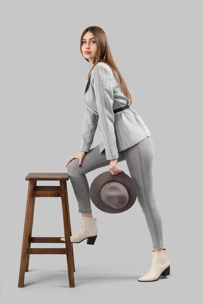 灰色背景下靠近凳子的时髦年轻女子 — 图库照片