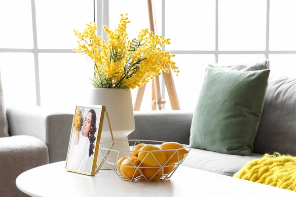 ミモザの花の花瓶 バスケットのレモンとリビングルームのコーヒーテーブルの上の女性の写真 — ストック写真