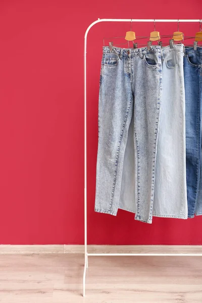 Cremalheira Com Jeans Elegantes Perto Parede Vermelha — Fotografia de Stock