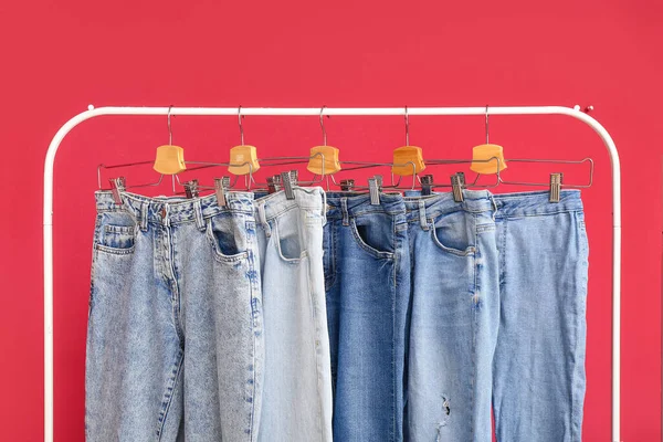 Rack Met Stijlvolle Jeans Rode Achtergrond Close — Stockfoto