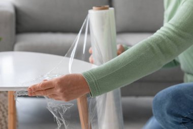 Olgun bir kadın, evinde streç film olan bir paket masası, yakın çekim.