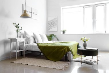 Işıl ışıl yatak odasının içinde rahat bir yatak odası ve pouf üzerinde narsis çiçekleri.